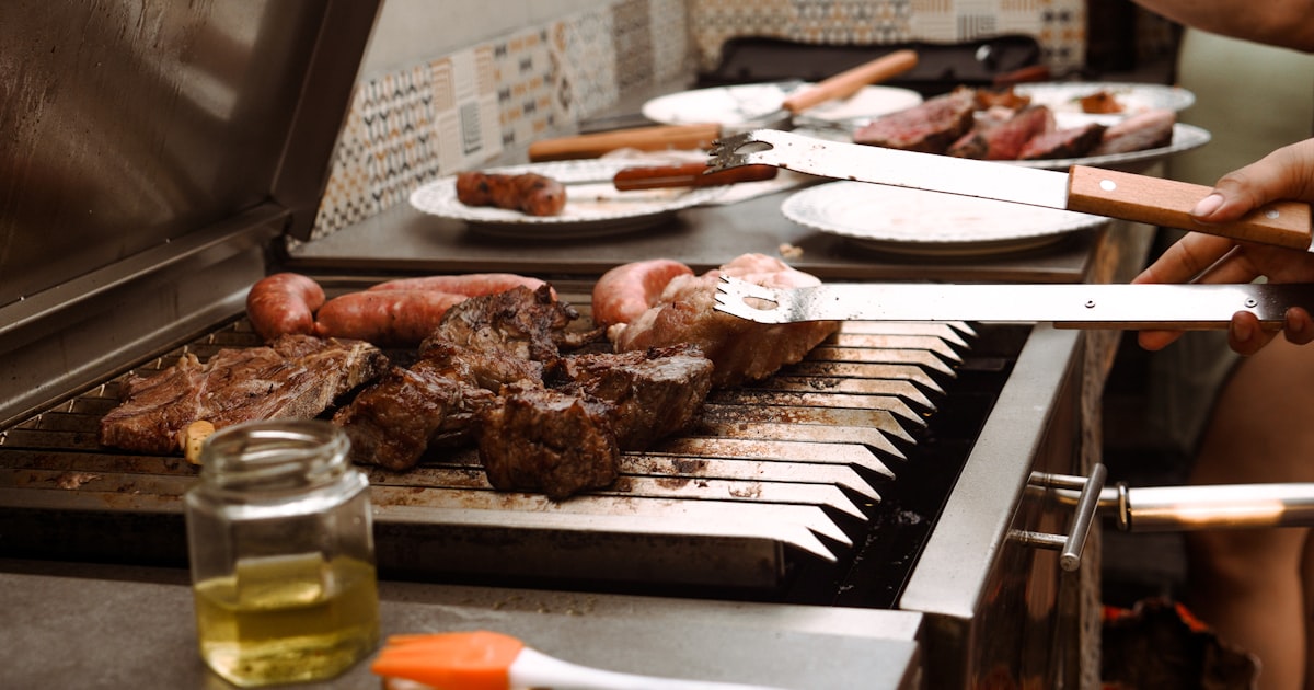 a person grilling meat on a grill with tongs — Clube Prime, Empório Família Rodrigues