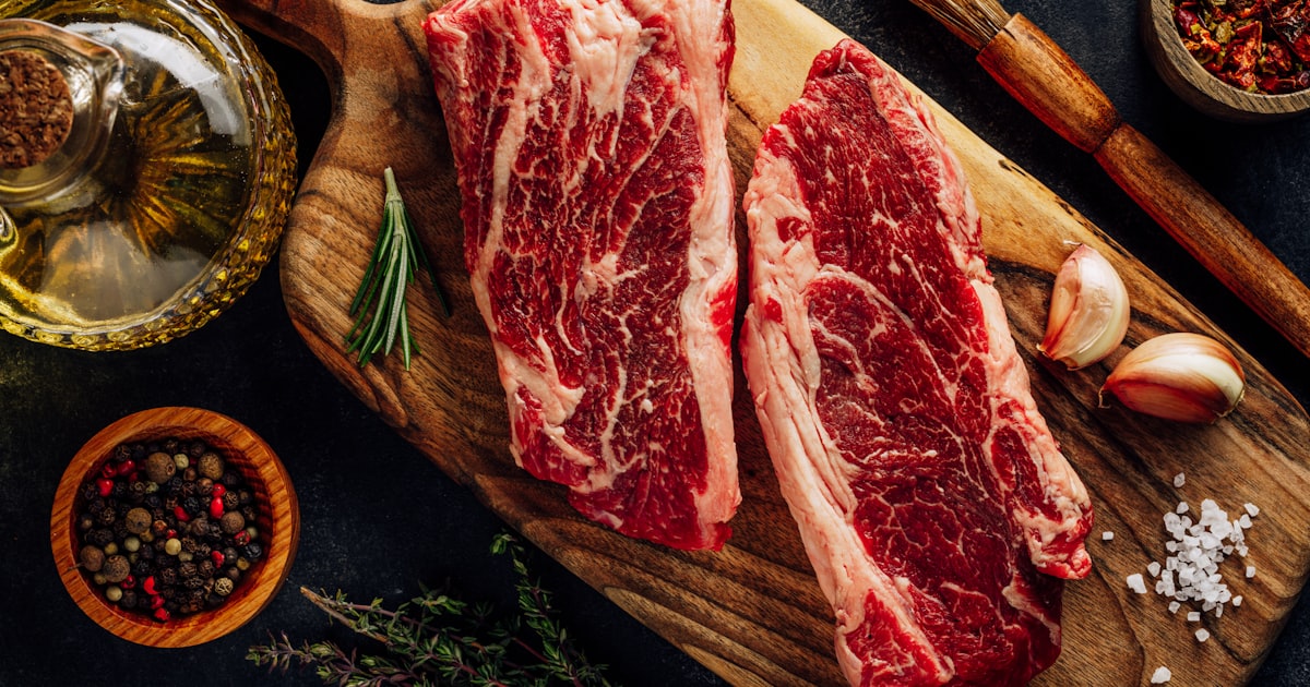 a slab of raw meat on a cutting board with vegetables and a bowl of sauce — Clube Prime, Empório Família Rodrigues